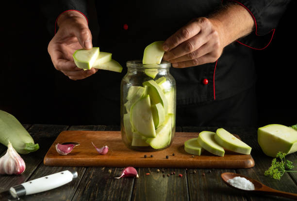 istock Chef hands filling jar with chopped vegetable marrow before canning with spices on kitchen table. Concept of pickling tasty zucchini 2168583008