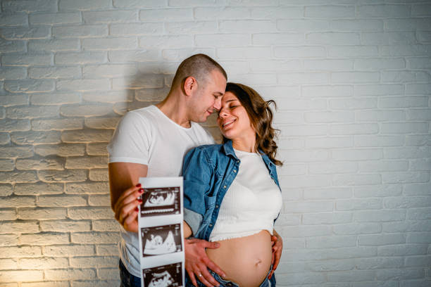 Expecting parents holding hands and a pair of baby shoes, symbolizing their anticipation for their child's arrival