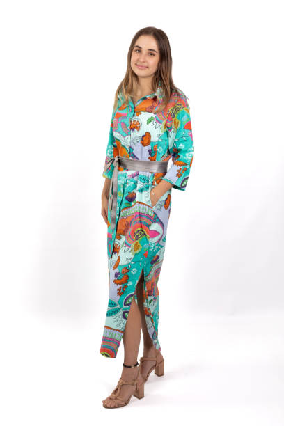 istock A young woman stands in a full-length image, wearing a brightly colored and bold patterned shirt dress against a crisp white background 2168595375