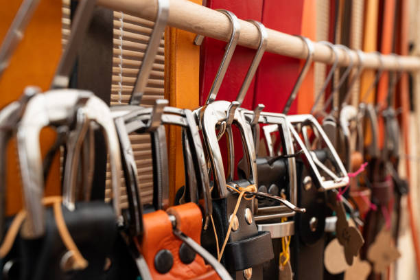 A row of belts hanging on a rack, some of which are leather. The belts are of various colors and styles, and they are all hanging on a rack