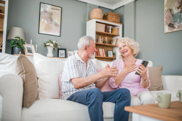 istock Happy mature couple using mobile phone while sitting on sofa and enjoying drinking coffee 2168599826