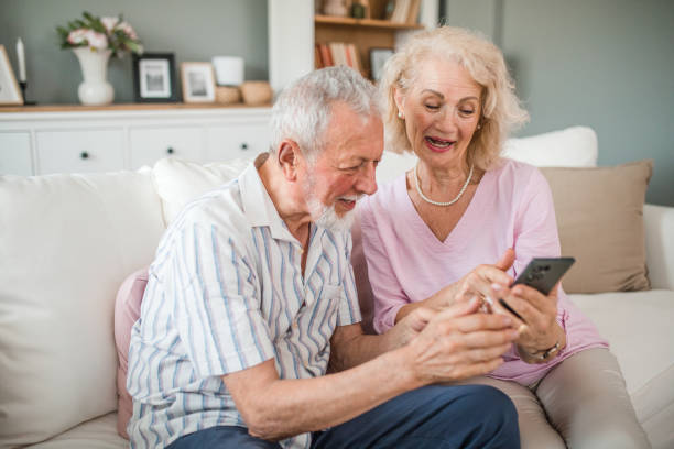 istock Happy senior couple using mobile phone while sitting in the living room 2168600033
