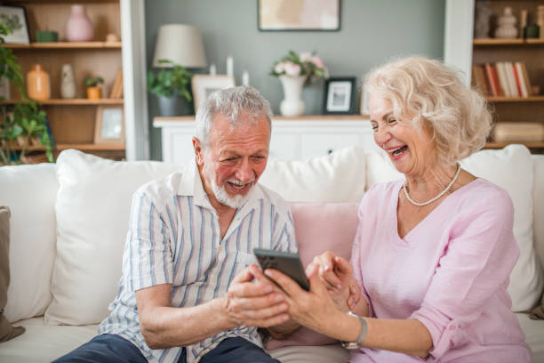istock Happy senior couple using mobile phone while sitting on sofa in living room 2168600112