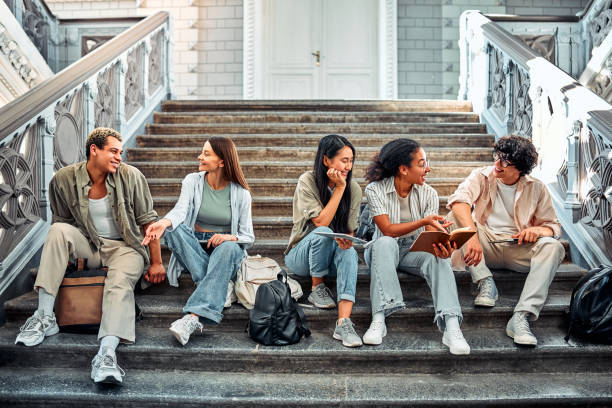 istock Multicultural students sitting together on the stairs and talking. They hold books, notebooks, backpacks and laptops. 2168600745