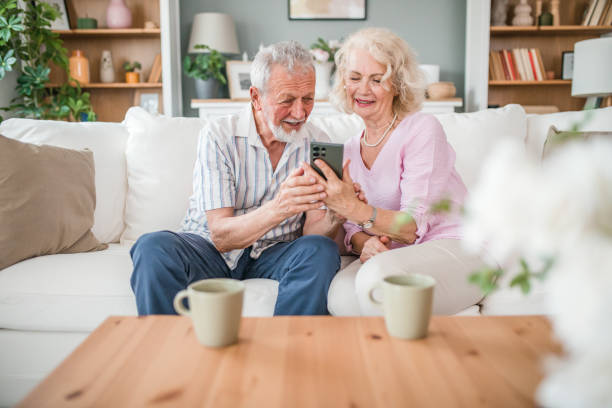 istock Senior couple using mobile phone while sitting on sofa and enjoying drinking coffee 2168601238