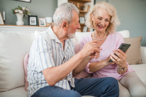 istock Smiling senior couple using mobile phone while sitting in the living room 2168601698