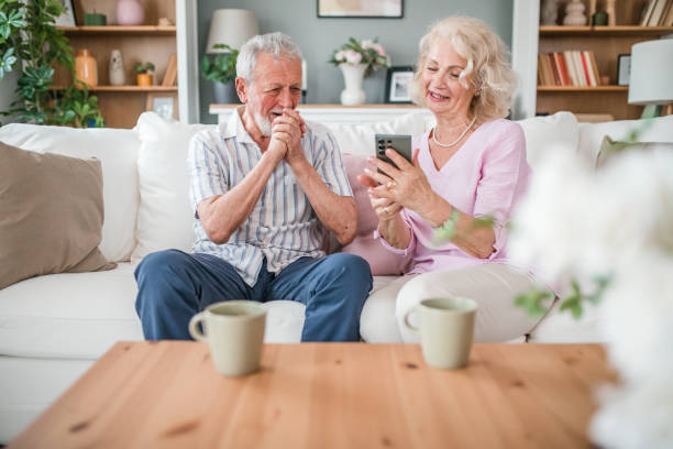 istock Smiling senior couple using mobile phone while sitting on sofa and enjoying drinking coffee 2168601743