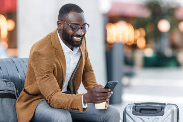 istock Smiling businessman using smart phone while waiting with luggage 2168610764