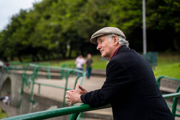 Retired man between 50-70 on a day in the park, breathing fresh air, walking, smiling, taking a little sun, enjoying his days off in retirement and enjoying admiring the landscape and people playing