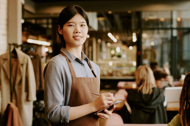 istock Smiling Asian Waitress Holding Notepad in Busy Cafe 2168616212