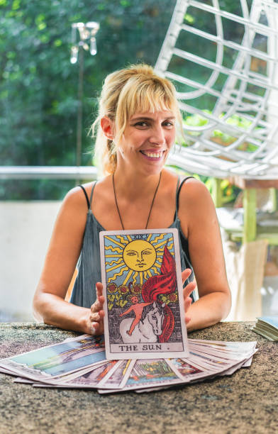 istock Tarot reader smiling at the camera while holding a giant card of The Sun. 2168617281