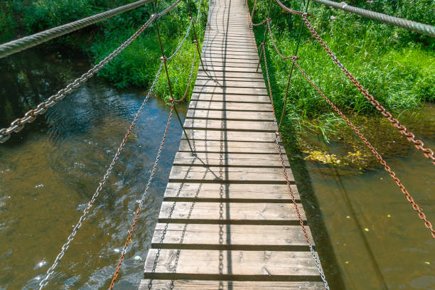 Narrow suspension wooden bridge across the Black Cheremosh River in the village of Verkhovyna. Rural summer landscape. Suspension bridges are one of the attractions of the Carpathians. Ukraine.