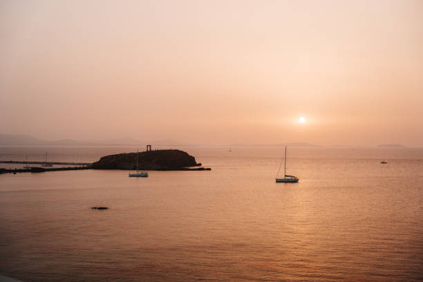 View of sailboat and the temple of apollo in the distance silhouetted at sunset in Naxos, Greece.