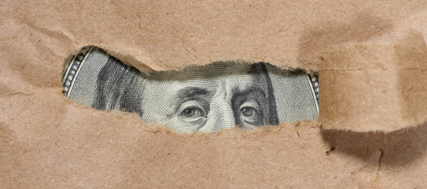 istock A piece of a hundred dollar bill is visible through a hole in th 2168631951