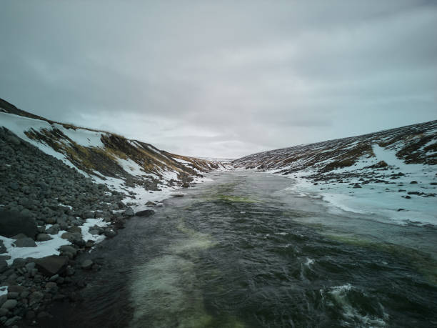 Powerful river carving its way through a snow covered valley, with a cloudy sky above