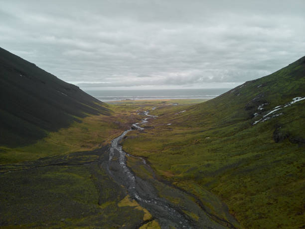 River is flowing between two mountains leading to the ocean on a cloudy day