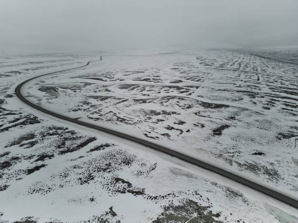 Aerial view of a winding asphalt road crossing a vast snowy landscape