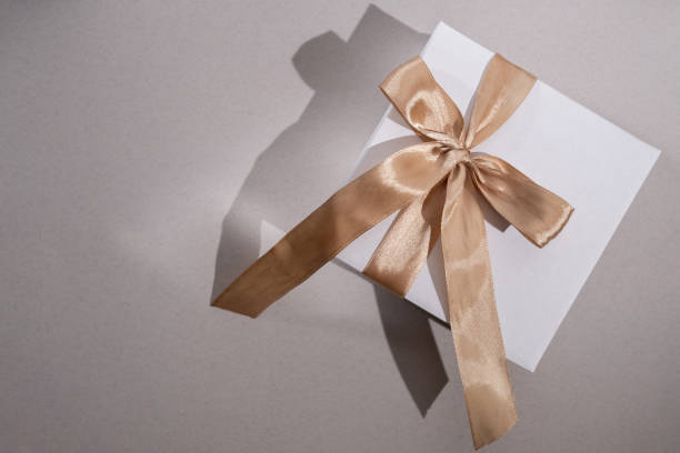 istock White box with gold bow and ribbons on color background. Gift box 2168641927