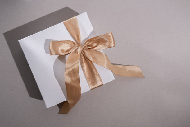 istock White box with gold bow and ribbons on color background. Gift box 2168641933