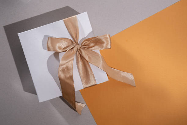 istock White box with gold bow and ribbons on color background. Gift box 2168641936