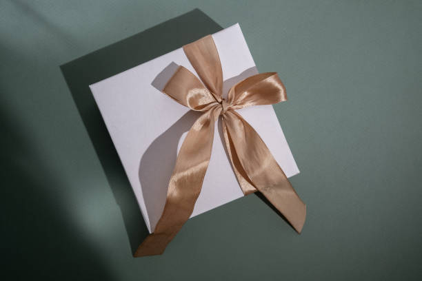 istock White box with gold bow and ribbons on color background. Gift box 2168641975