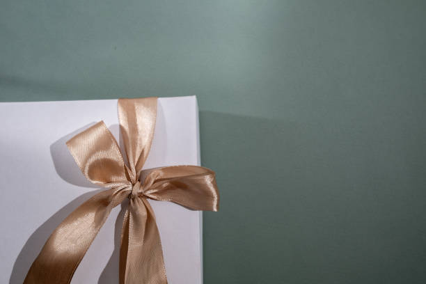 istock White box with gold bow and ribbons on color background. Gift box 2168641976