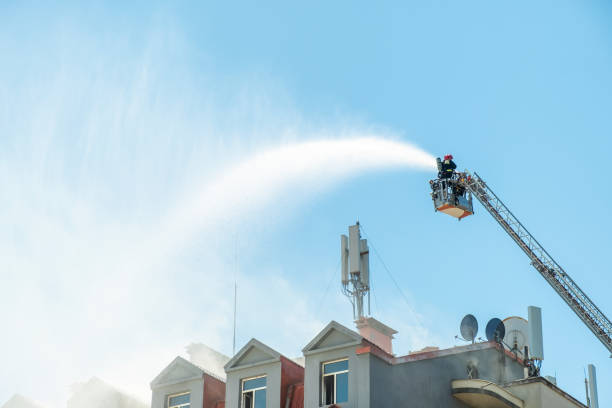 istock Firefighters extinguish burning house using extended ladder equipped with water hose to spray water onto the building roof with smoke. Fireman extinguishing fire in the city 2168642632