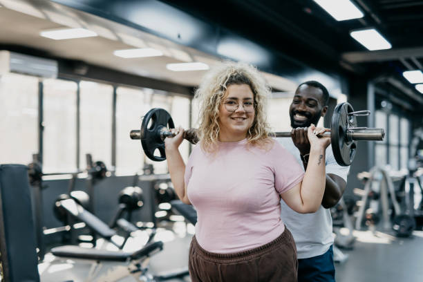 istock Woman lifting weights at gym with help from trainer. 2168645442