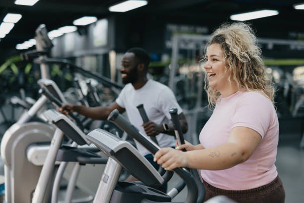 Gym workout scene: Woman and trainer on ellipticals.