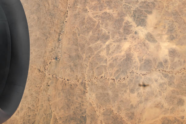 Aerial view of arid climate dried lands sandy reg with dried out plants, small mountain reliefs and river pattern. Sunny day, the airplane shadow casts on the ground afar.