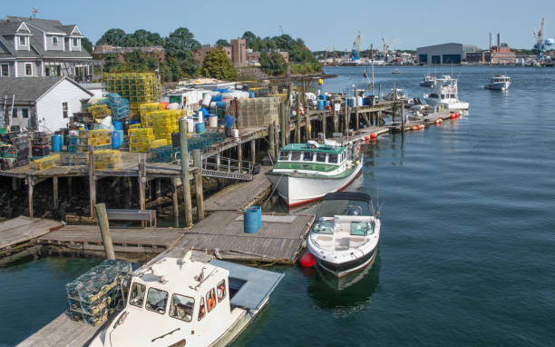 Fishing boats dock beside stacks of lobster traps at a wharf in Portsmouth, New Hampshire.