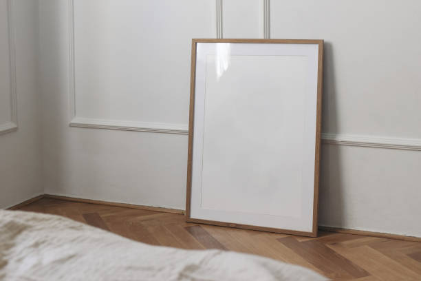 istock Vertical thin picture frame mount mockup. Empty wooden frame poster mock-up template on oak wooden parquet floor. White wall background, stucco decor. Minimal Scandinavian interior, blurred bed sofa 2168663853