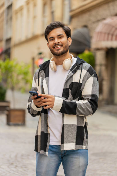 istock Indian young man using smartphone text messages browsing internet smiling at camera outdoors 2168676674