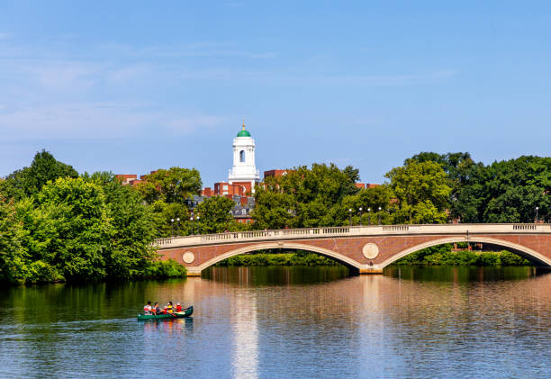 NYC NY USA May 5 2018: As strollers enjoy Bow Bridge and boaters row about the boat lake in sunshine from southwest, ominous clouds appear in the north. \n\nBow Bridge was designed by Calvert Vaux and Jacob Wrey Mould and completed in 1862. It is one of the first cast-iron bridges in the United States. Bow Bridge is located in the center of Central Park, spanning across The Lake. It connects the Ramble and the Central Park Mall, making it a key link between these popular areas. Bow Bridge is a beloved landmark and a favorite spot for both tourists and locals. Its romantic and picturesque setting makes it a popular location for wedding proposals, photoshoots, and scenes in films and television shows.