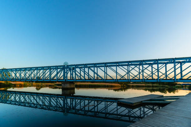 Former train track above a river with wooden dock, near marsh, with shiny water reflection during blue hour using a filter