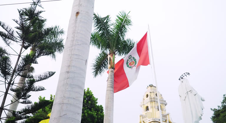 Beautiful slow motion shot of the flag of Peru flying in a town square during a cloudy day.