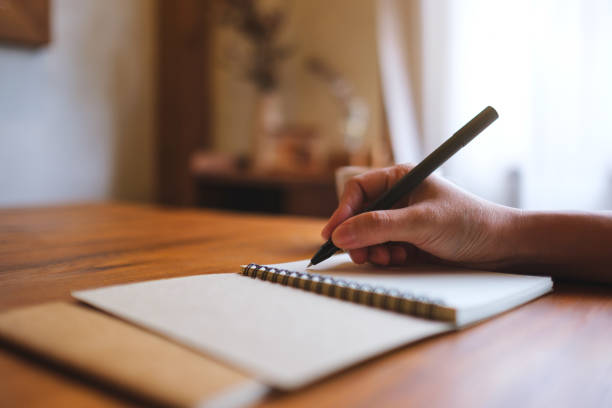 istock Closeup image of a hand holding a pen and writing on notebook on wooden table 2168702329