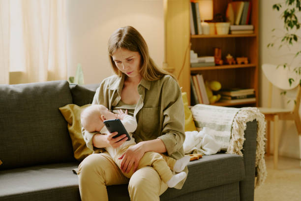 istock Caring Mother Holding Baby While Looking at Smartphone 2168710744
