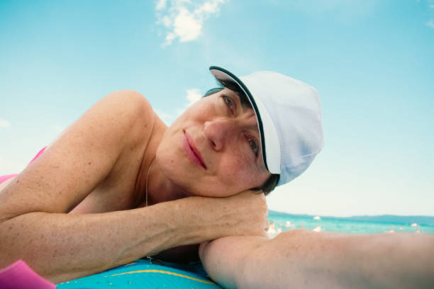portrait of a beautiful natural middle-aged woman with a white cap, lying on the beach, enjoying and contentedly looking at the sky, the upper body is visible o and the sky
