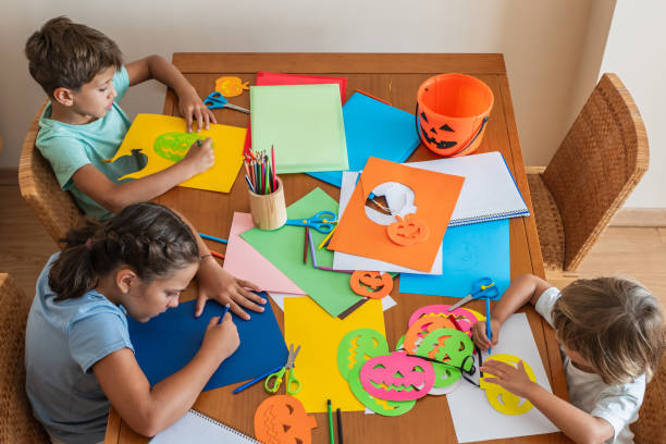 istock Children Working On Halloween Art Projects At A Table, Using Scissors And Colored Paper To Create Festive Decorations. Kids Making Halloween Crafts At Home 2168726706