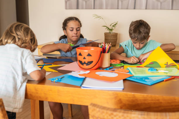 istock Three Children Crafting Halloween Decorations At A Table, Creating Colorful Paper Pumpkins And Enjoying A Fun Group Activity. Halloween Crafts At Home 2168726749