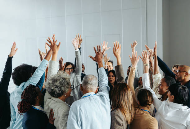 istock Diverse group of colleagues raising hands in a team-building exercise indoors 2168749916
