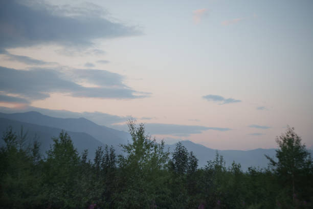 A tranquil scene of misty mountains and green fields at dawn, with a soft pastel sky overhead, creating a serene and peaceful atmosphere.