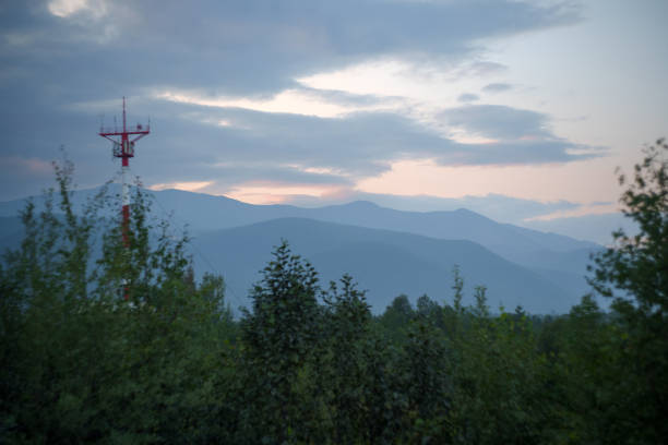 A misty mountain landscape at dawn featuring lush greenery and a red radio tower under a cloudy sky, creating a tranquil and serene atmosphere.