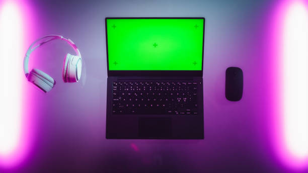 Top Down View of a Laptop Computer with Mock Up Green Screen Chromakey Display with Motion Trackers Standing on an Neon Desk Next to Wireless Mouse and Headphones. Online Gaming Concept