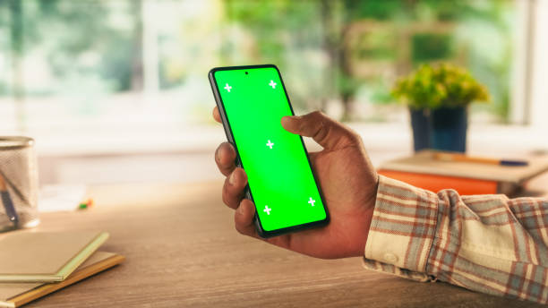 istock Anonymous Man Holding a Smartphone Device, Reading Articles on Mobile Phone with Green Screen Mock Up Display. Photo Template with Placeholder for Digital Marketing and Business Promotions 2168766303