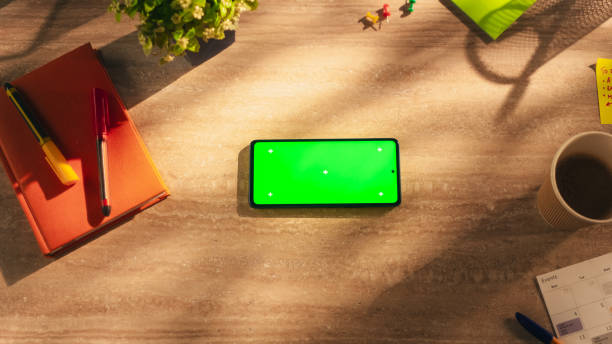 istock Top Down View of a Smartphone with Mock Up Green Screen Display. Phone Lying Horizontally on a Wooden Table in a Creative Office. Template for Digital Marketing, Social Media and Screen Replacements 2168769448