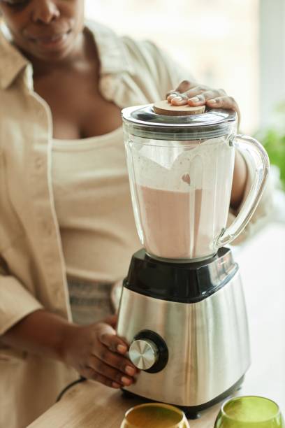 istock Black Woman Using Kitchen Blender Mixing Ingredients on Beige Counter 2168777379