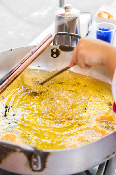 A woman is cooking picarones in a pan. The food is being cooked on a stick
