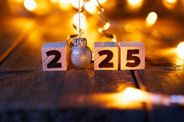 istock Festive New Year 2025 concept with wooden blocks arranged on a rustic table surrounded by warm glowing fairy lights, highlighting a sparkling silver ornament in place of the zero. 2168800675
